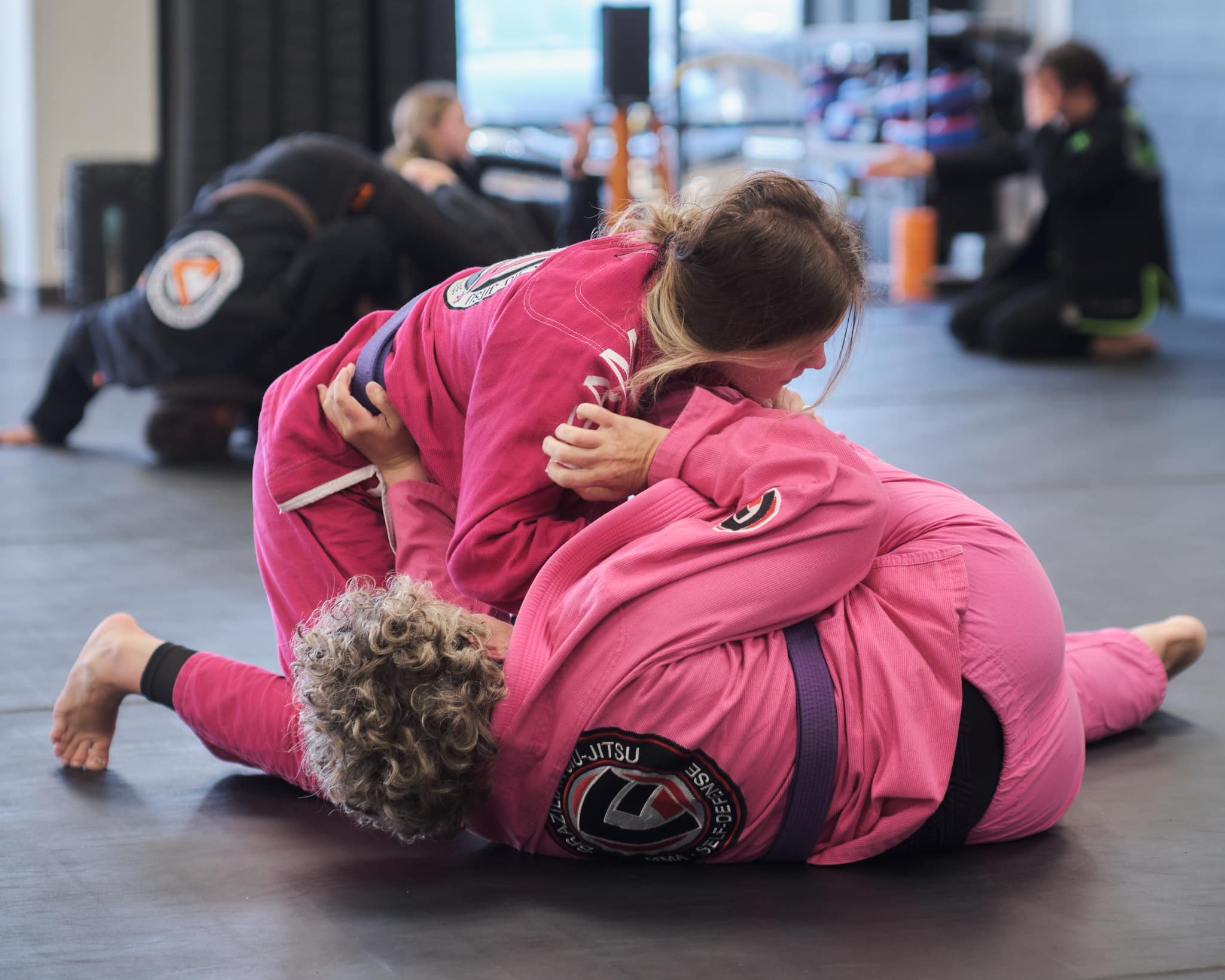 two Gracie United - Team Jucao Red River students grappling at jiu-jitsu class in pink gi